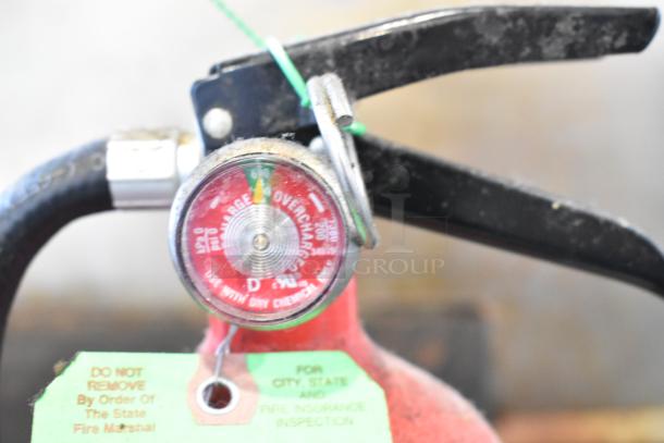 Close-up of a Kidde fire extinguisher gauge showing charge level with inspection tag. Condition appears used.
