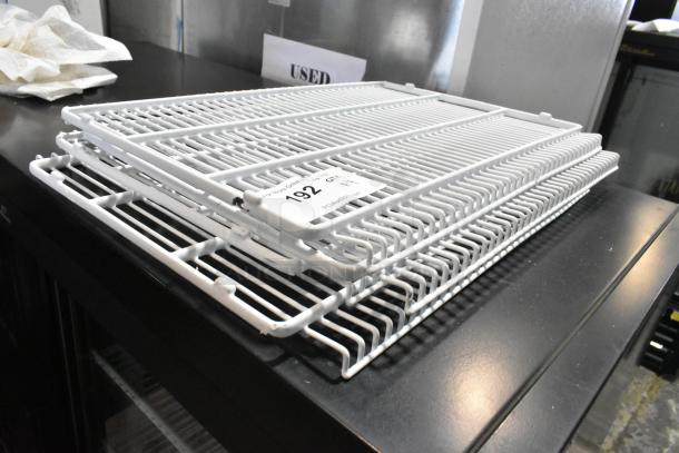 Lot of 4 white poly-coated racks, gently used, stacked on a table. Each rack features a durable wire design.