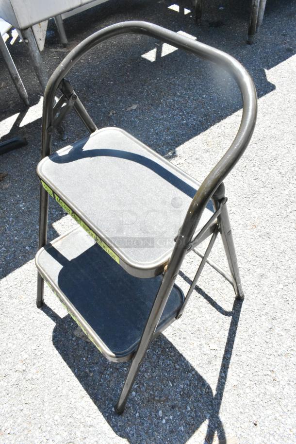 Two-step folding ladder with black steps and metal frame. Condition appears lightly used. Safety label visible on side.