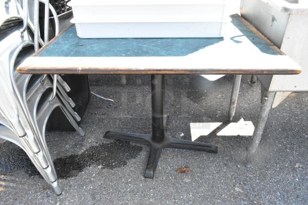 Green table with wood-patterned edge, set on a black metal base. Shows signs of use; sturdy design.