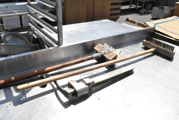 Stainless steel table with two grill brushes, can opener, metal under shelf, and commercial casters.