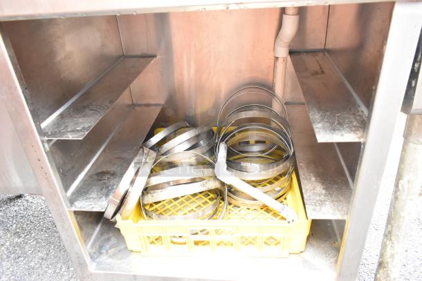 Stainless steel shelves inside commercial kitchen rack, showing metal rings and a PVC pipe in a yellow crate.