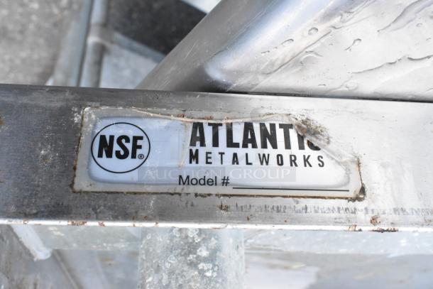Atlantic Metalworks stainless steel table with metal under shelf, labeled NSF, worn condition.