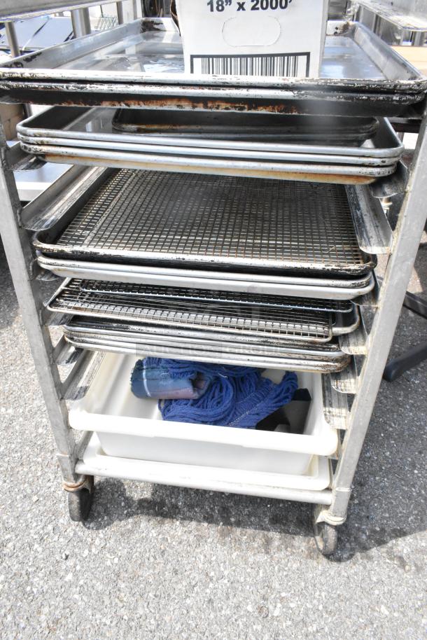 Metal commercial pan transport rack on casters with 12 metal baking pans, showing signs of use, includes storage bin.