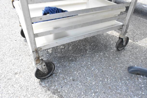 Metal commercial pan transport rack with casters, containing 12 metal baking pans. Suitable for bakery use, shows wear.
