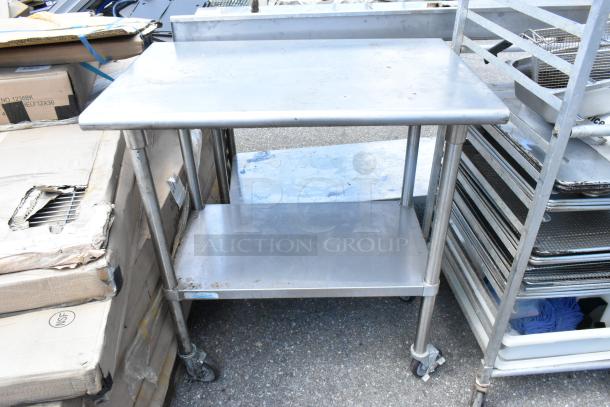 Stainless steel table with metal under shelf, commercial casters, in fair condition, ideal for kitchen use.