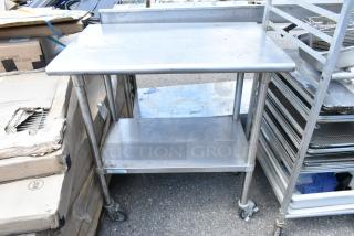 Stainless steel table with metal under shelf, commercial casters, in fair condition, ideal for kitchen use.
