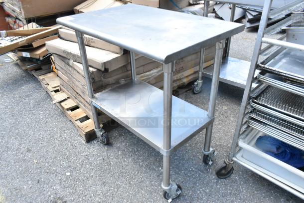 Stainless steel table with metal under shelf, on commercial casters. Light wear, suitable for kitchen or industrial use.