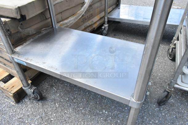 Stainless steel table with metal under shelf and commercial casters, showing minor wear. Ideal for commercial use.
