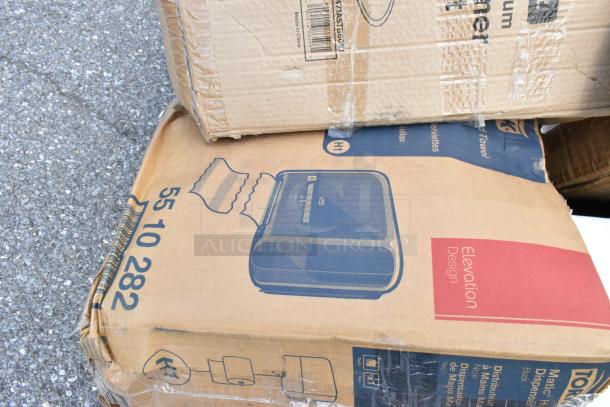 Cardboard boxes with various items, including a Tork hand towel dispenser in Elevation Design. Some wear visible.