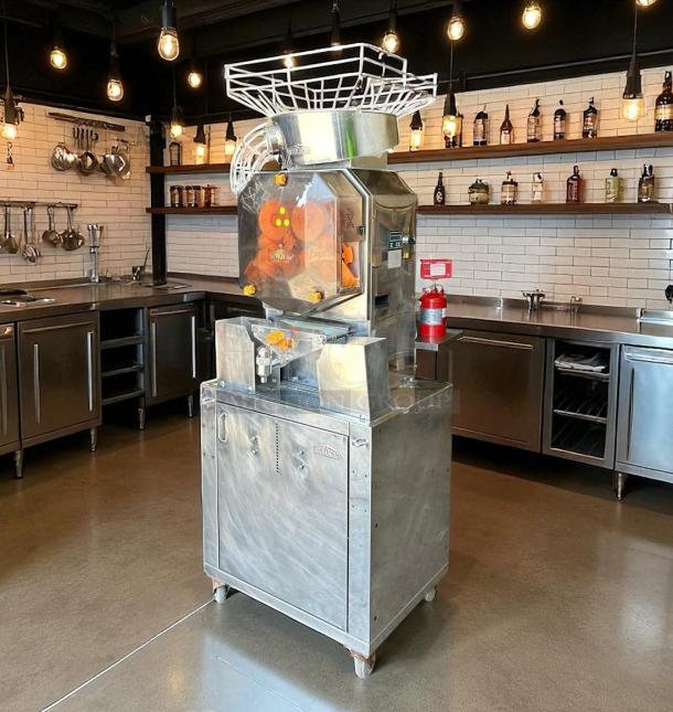 Industrial juice extractor in a stainless steel kitchen, featuring a modern design with visible components and safety labels.