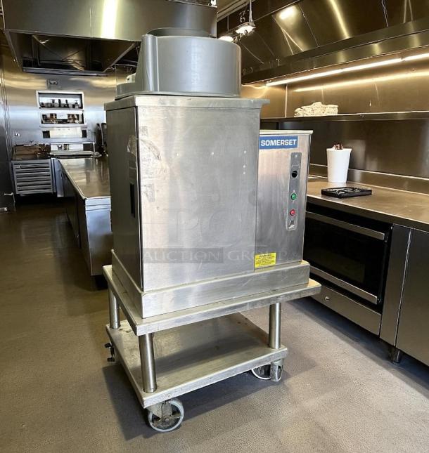 Somerset dough sheeter on wheels in industrial kitchen, stainless steel, visible buttons and warning label, good condition.