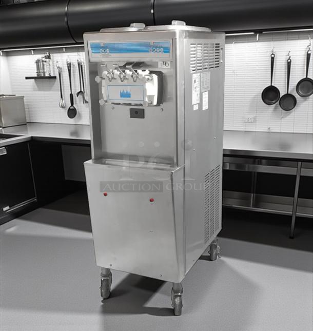 Commercial soft serve ice cream machine, stainless steel, model 138, three spouts, caster wheels, visible control panel.