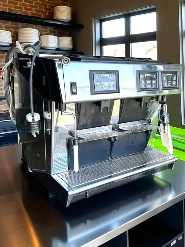 Commercial espresso machine with dual-group heads, digital displays, and steam wands. Stainless steel, excellent condition.