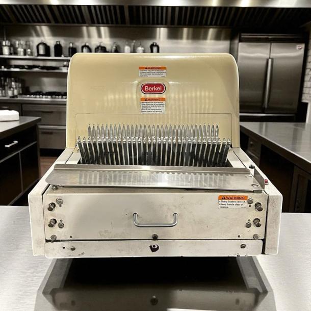 Berkel commercial bread slicer, model 149. Features stainless steel blades, visible warning labels, used condition.