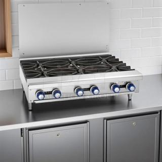 Stainless steel countertop gas range with six burners and blue control knobs. Features a backsplash and robust design.