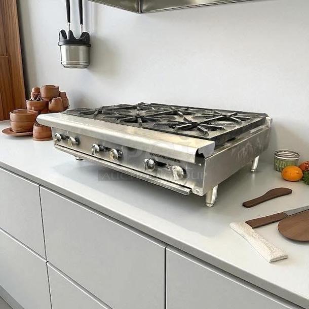 Stainless steel countertop gas range with four burners, shown in a kitchen setting, in good condition.