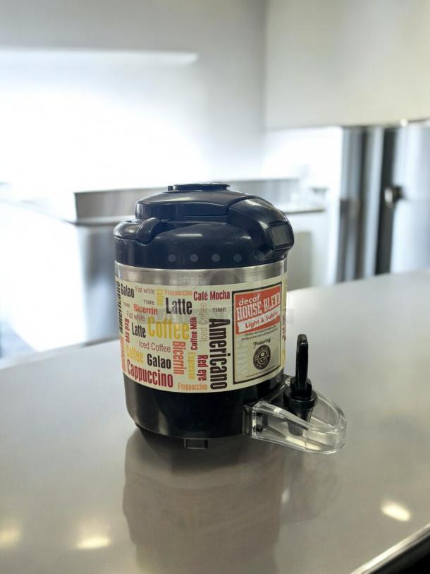 Black insulated coffee airpot dispenser in excellent condition, fully tested, featuring colorful beverage label.