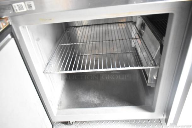 Inside view of a food trailer with a metal wire shelving unit. Visible appliances include coolers and freezers.