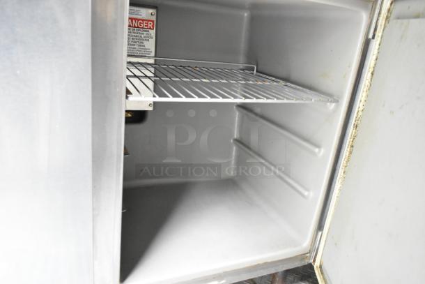 Interior of a stainless steel cooler in a mobile kitchen trailer, featuring a wire shelf and warning label. Clean and ready for use.