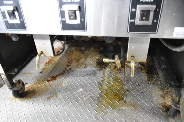 Grease-splattered metal floor under fryer controls in a used food trailer kitchen, showing signs of wear and operation.
