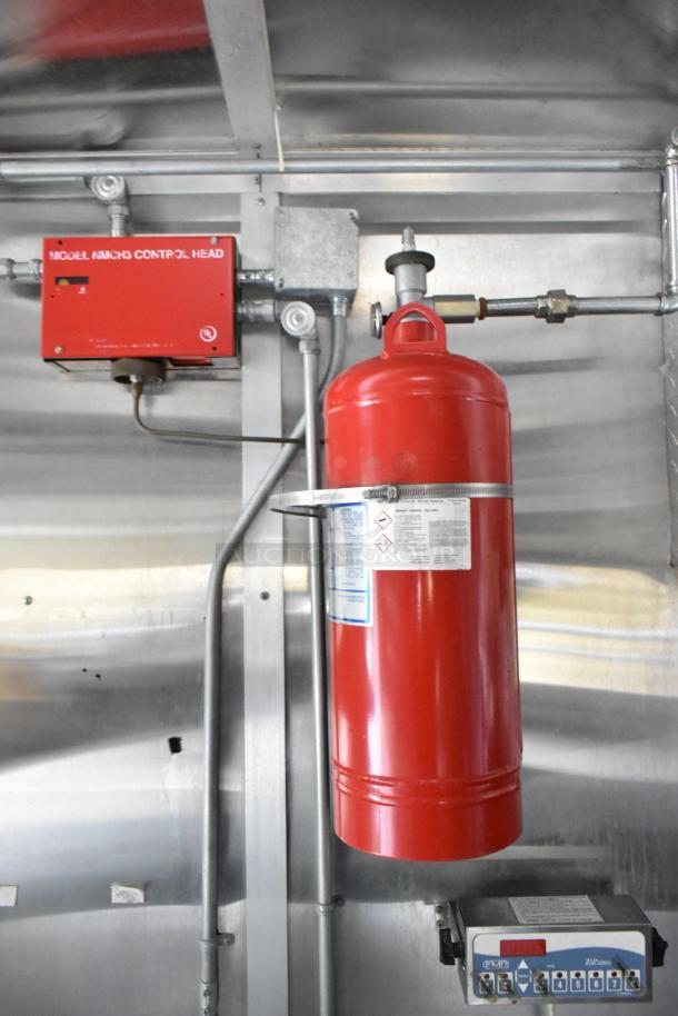 Red fire suppression system with control panel inside a fully outfitted mobile kitchen trailer, ready for operation.
