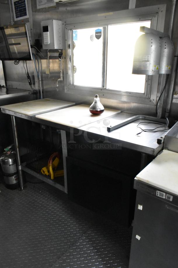 Former Popeyes food trailer interior with stainless steel prep tables, overhead lights, a safety extinguisher, and visible wiring.