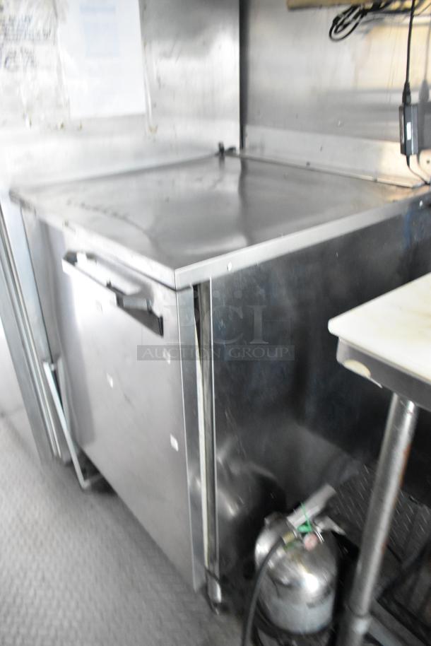 Mobile kitchen interior showing stainless steel prep table and cooler; features prepping essentials for efficiency.