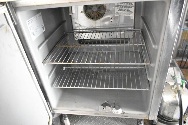 Interior view of a stainless steel food trailer cooler with wire shelves. Labels advise on safe refrigerant use.