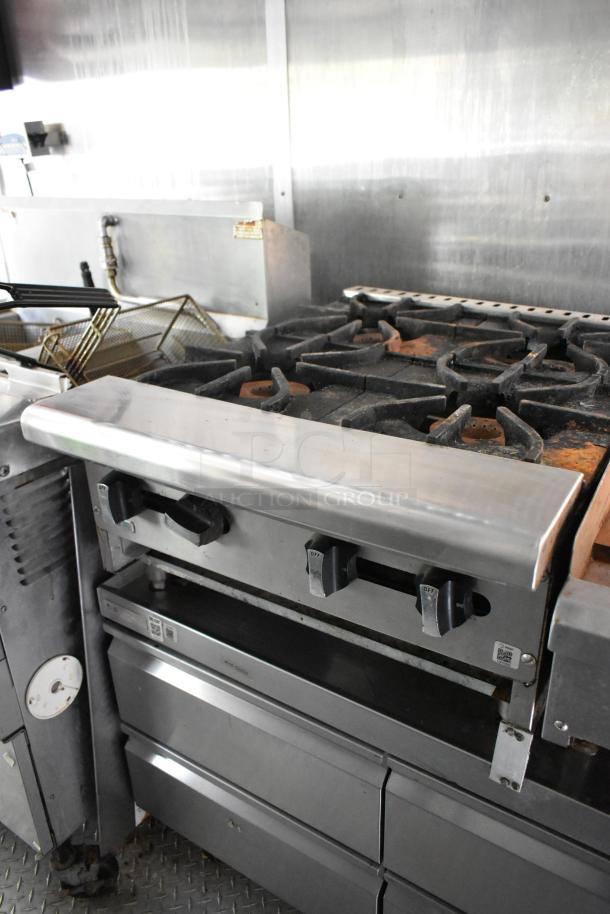 Mobile kitchen trailer with stove, knobs, grease hood, fry baskets, and metallic surfaces. Well-equipped for cooking.
