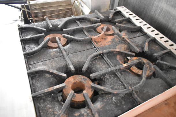 Four-burner stove with cast iron grates in used condition, part of a fully outfitted mobile kitchen trailer.