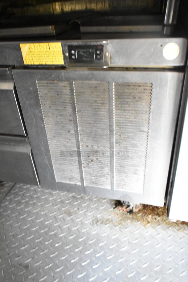 Food trailer interior showing metal appliance with vented door and control panel, moderate wear. Warning label visible.