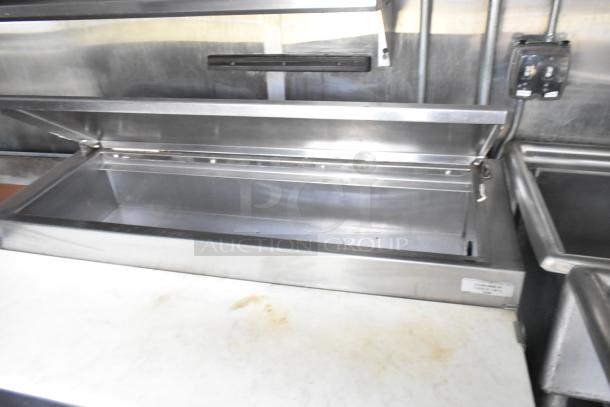Stainless steel food prep area inside a former Popeyes food trailer, featuring open storage compartment.