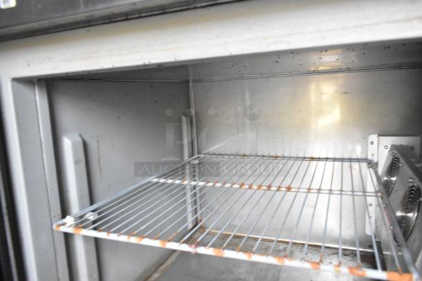 Interior view of a stainless steel cooler with wire shelving, showing signs of use. Ideal for mobile kitchen setup.
