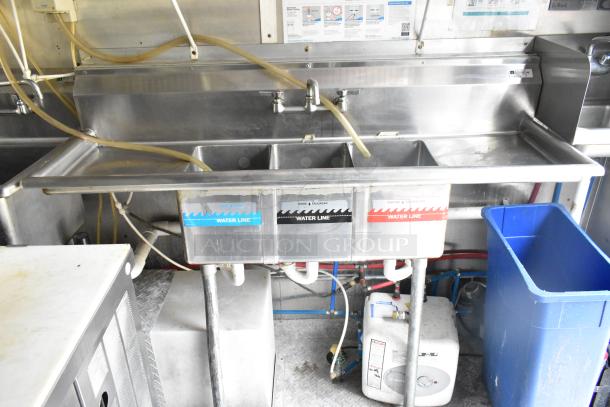 Stainless steel triple sink in mobile kitchen. Labels indicate water lines for wash, rinse, and sanitize. Clean condition.