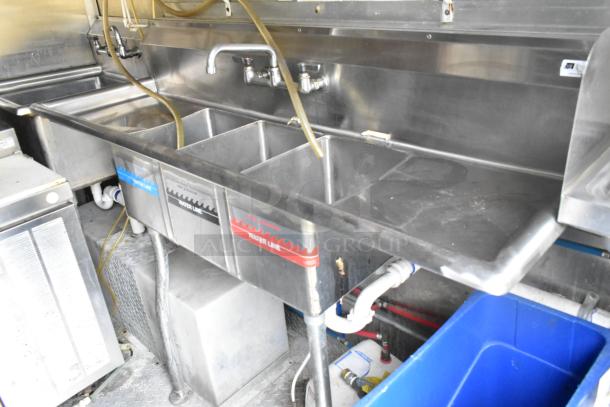 Stainless steel commercial kitchen sink in a fully outfitted mobile food trailer. Includes labeled water lines.