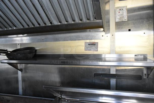 Fully outfitted mobile kitchen trailer interior with grease hood, shelving, and visible labels. Equipped for food service.