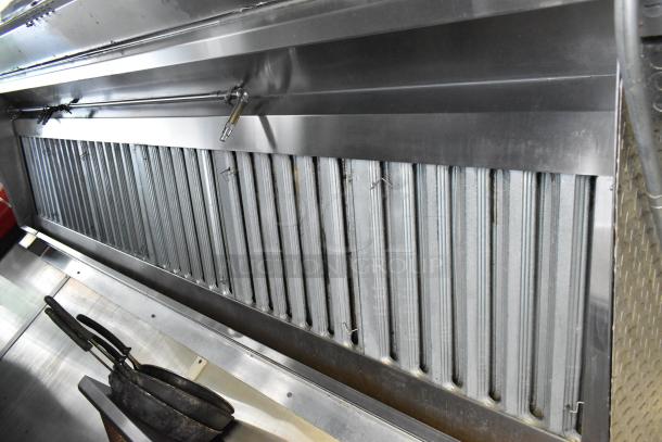 Stainless steel grease hood inside a mobile kitchen trailer with cooking utensils and industrial design.