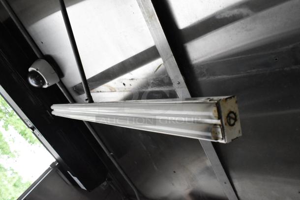 Interior view of a former Popeyes food trailer, showing ceiling fixture and surveillance camera. Steel structure visible.