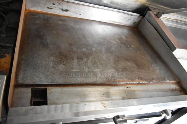 Flat top grill inside a mobile kitchen trailer, showing signs of use, with a smooth metal surface and grease catch tray.