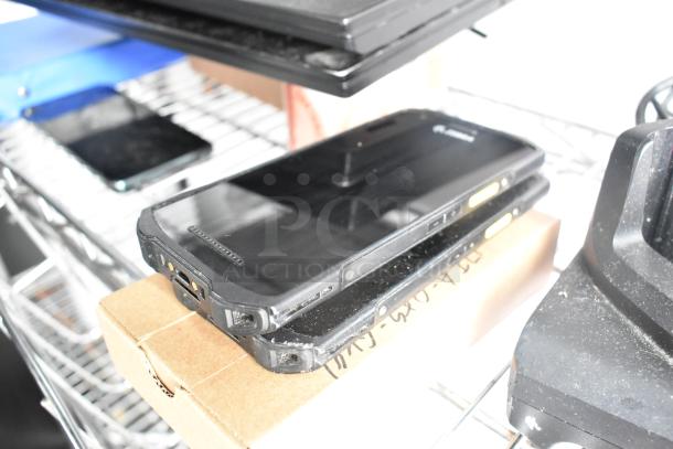 Black electronic devices stacked on a cardboard box on a metal shelf, next to other tech equipment.