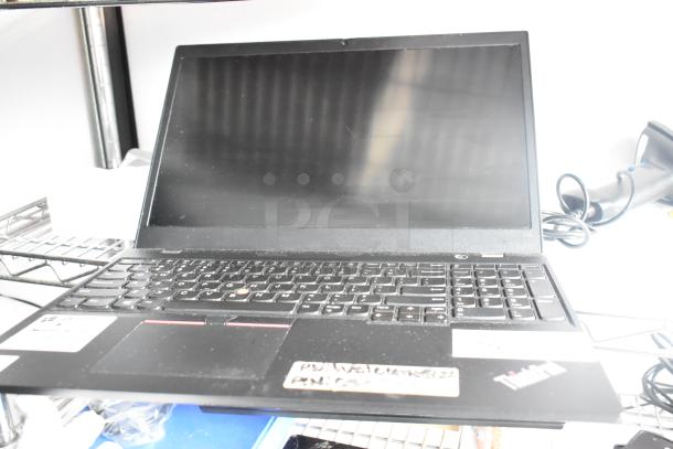A black laptop with a full keyboard and screen, featuring visible stickers and cables, resting on a metal shelf.