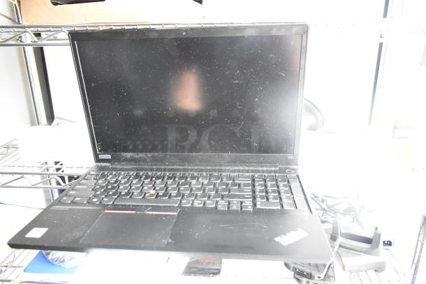 Laptop with partially visible branding and keyboard, placed on a metal shelf. Screen is off, showing some dust.