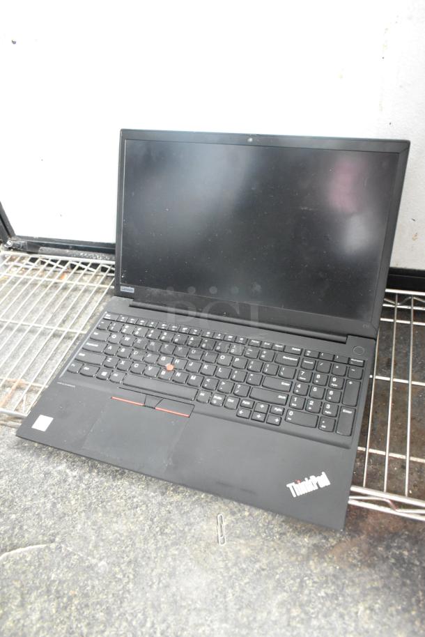Black Lenovo ThinkPad laptop with a visible keyboard and screen, placed on a wire shelf.