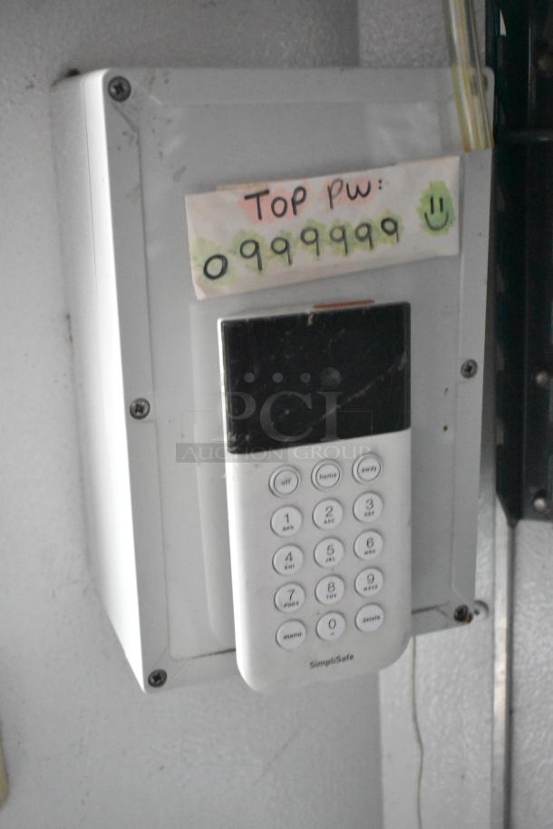 Security keypad labeled "SimpliSafe" mounted on a wall, with a note displaying a password.
