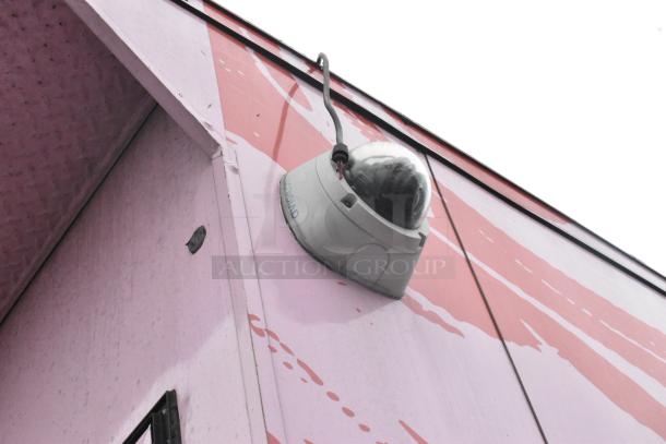 Depicts an outdoor part of a surveillance camera installed on a pink and red wall. Not relevant to the described food trailer.
