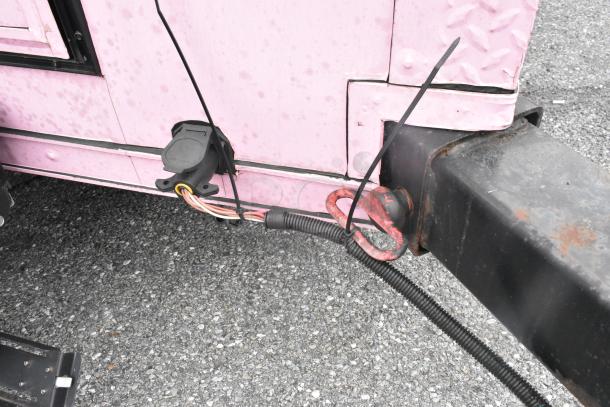 Close-up of a 2020 Goodees food trailer hitch showing electrical connections and part of a pink trailer exterior.
