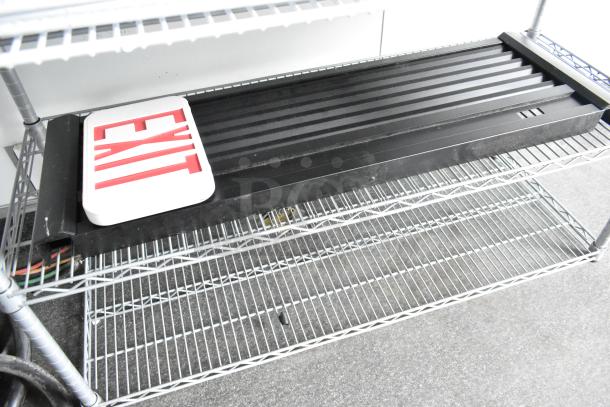 Steel wire shelving unit with black plastic grate and red "EXIT" sign. Items appear in used condition.