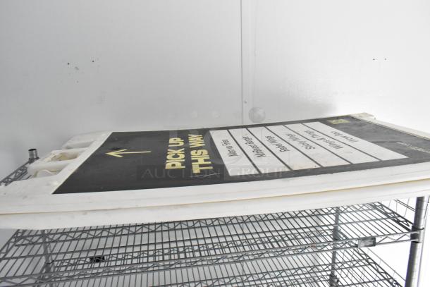 Stacked metal shelving unit with a black and white sign labeled "Pick Up This Way" at the top.