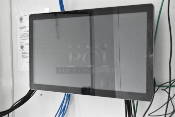 Mounted black screen with cables against a white wall, accompanied by visible paperwork.